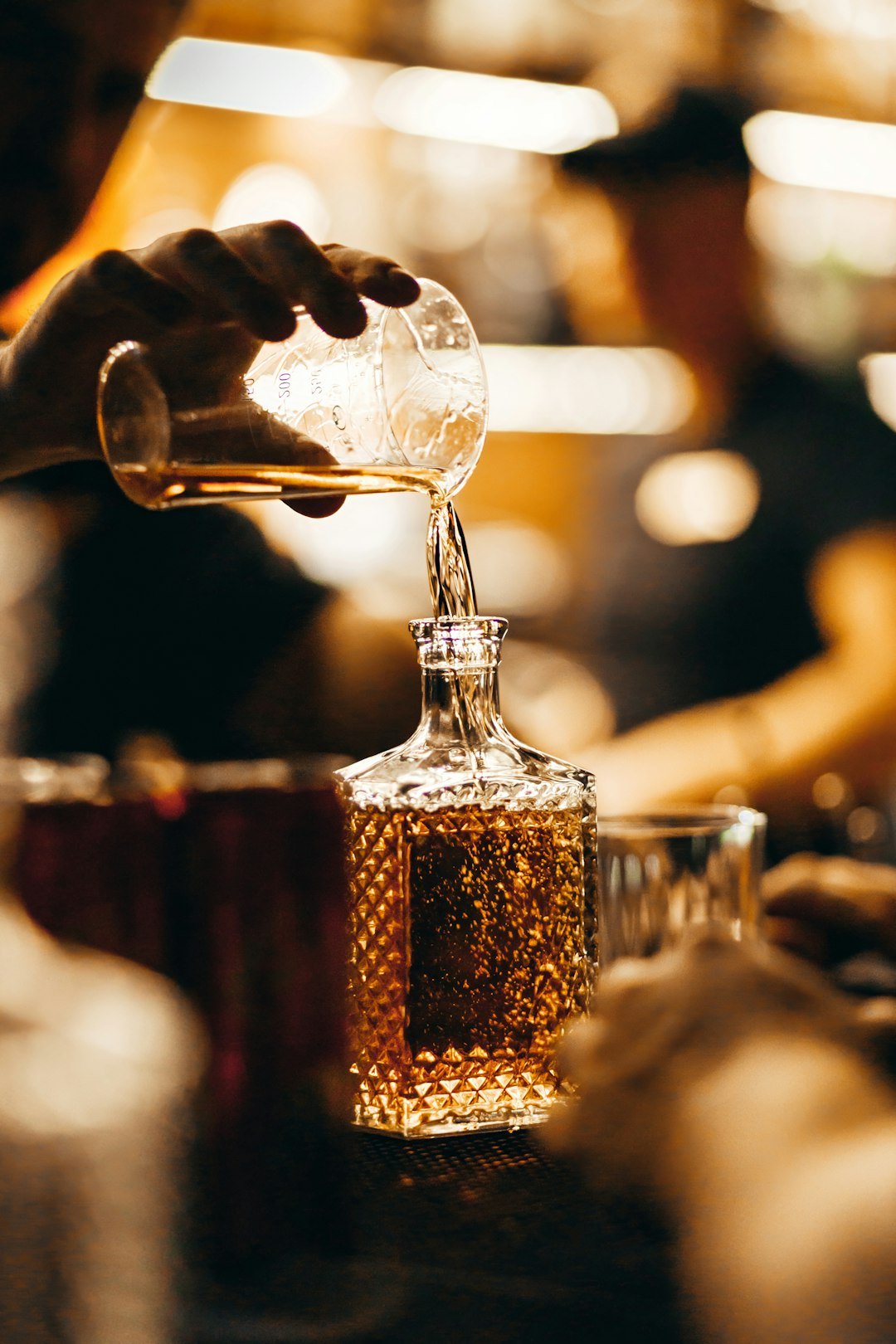 A bartender pours whiskey from a measuring glass into a decanter.